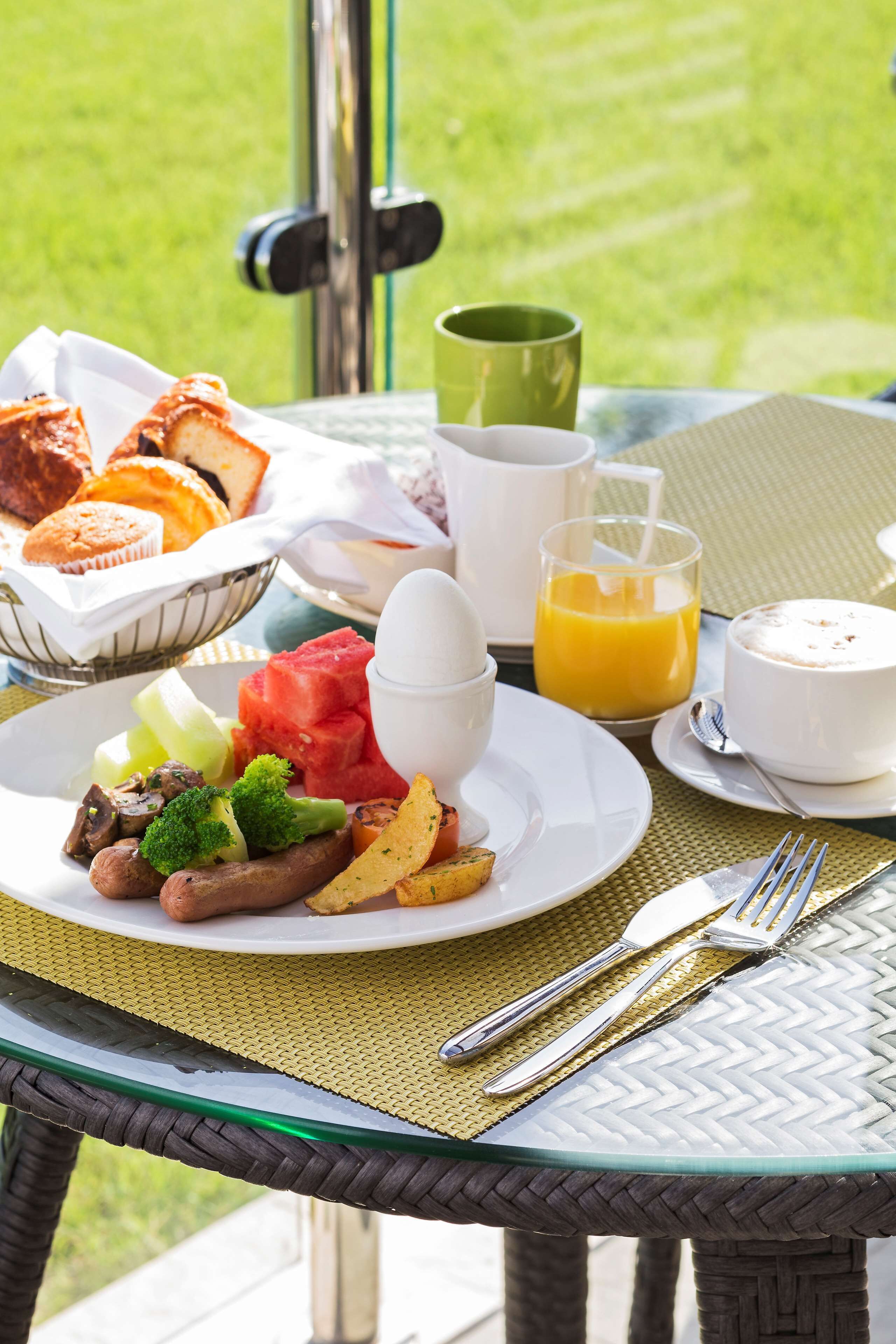 A breakfast setting with a plate of food, a glass of orange juice, and a cup on a table outdoors.