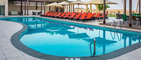 A swimming pool with lounge chairs and umbrellas, surrounded by a covered patio area.