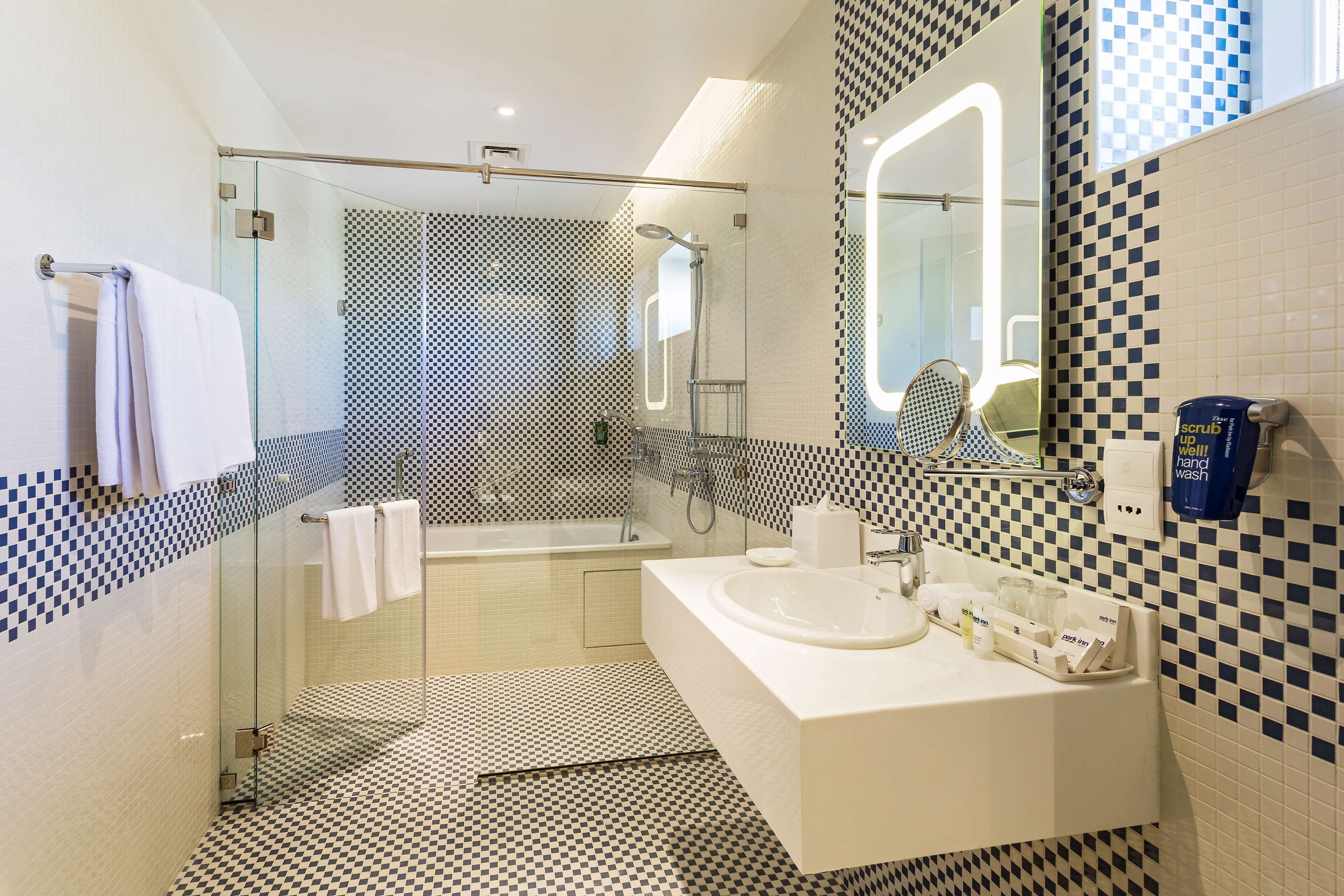 Un baño moderno con cabina de ducha de vidrio, bañera y lavamanos blanco con artículos de aseo.
