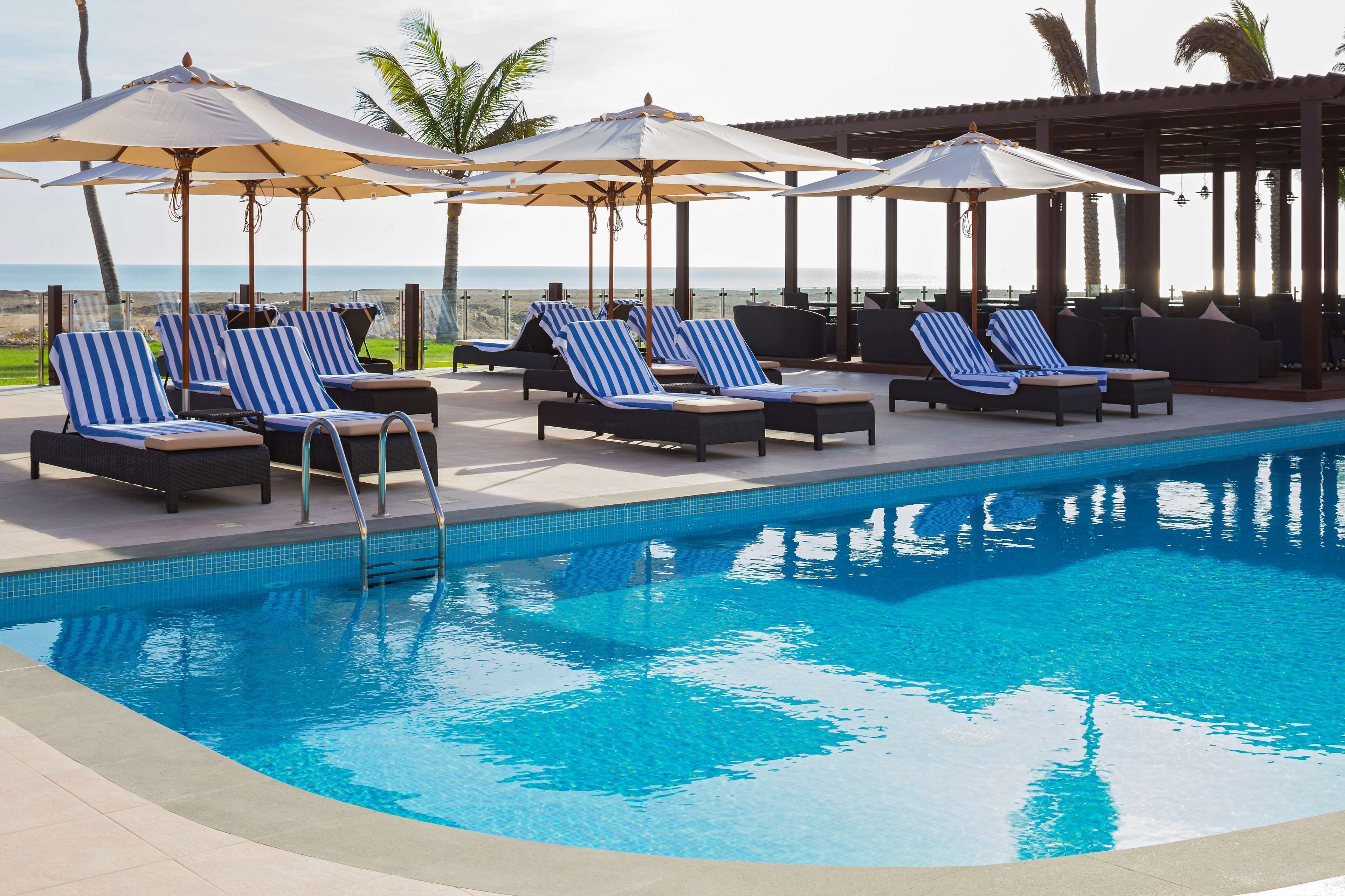 Un espace piscine doté de chaises longues et de parasols, offrant une vue dégagée sur l’océan, et dont le bord est revêtu de carrelage.