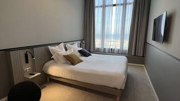 Une chambre d’hôtel moderne équipée d’un grand lit, d’un bureau, d’une chaise, d’un téléviseur à écran plat et d’un luminaire au plafond.