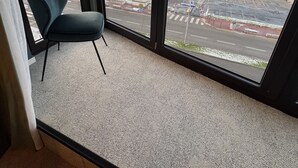 A room with a large window offering a view of a parking lot and a beach. -  L'Echappée - Hôtel Casino Dieppe (Dieppe)