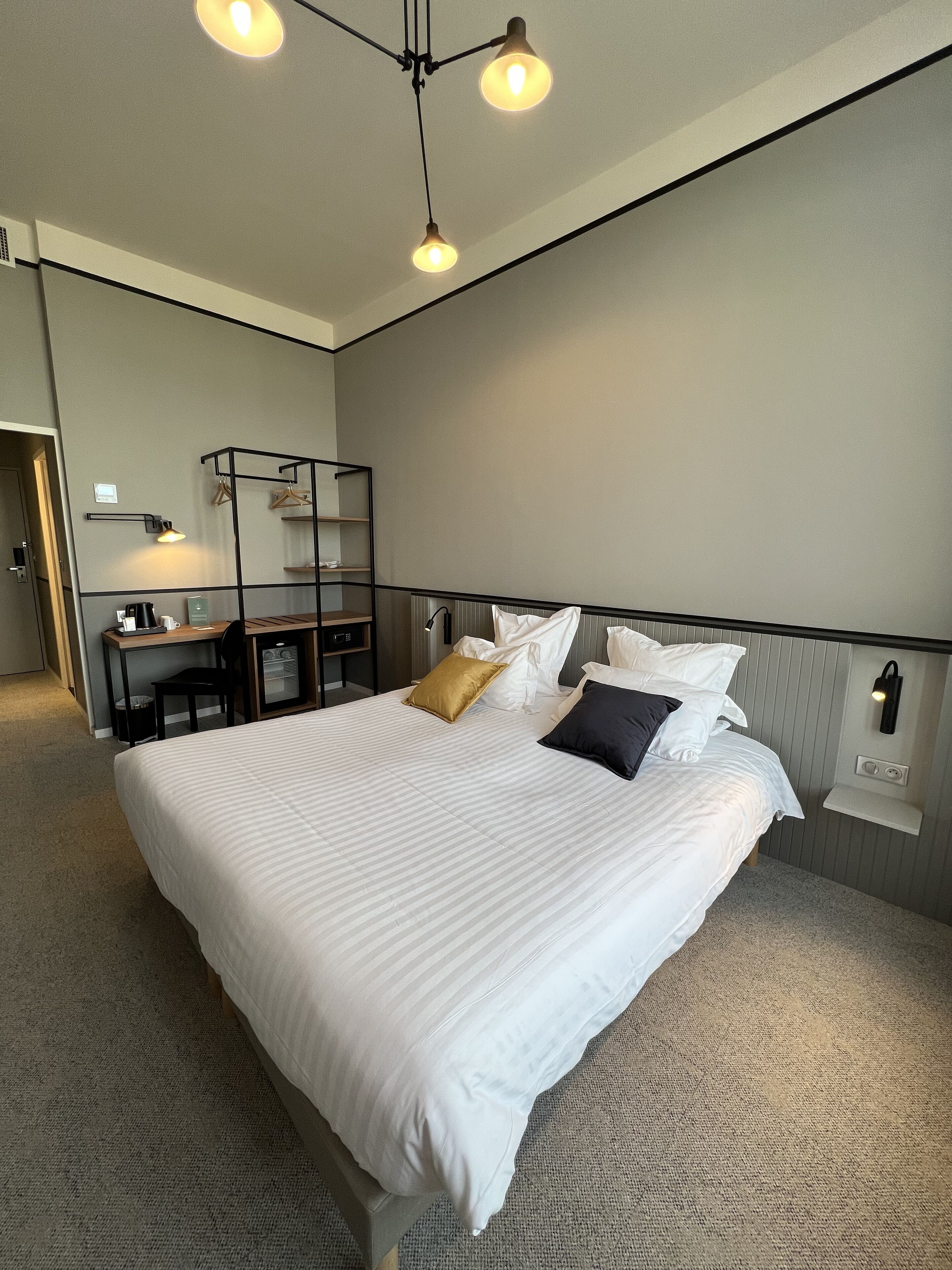 A neatly arranged hotel room with a large bed, bedside tables, a desk, and a hanging light fixture.