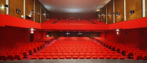 Un teatro con asientos rojos y un escenario central.