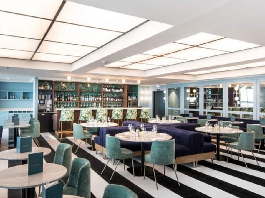 A modern restaurant with a high ceiling, striped floor, and a variety of seating options including round tables and sofas.