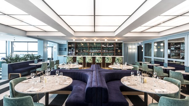 A modern restaurant with a central seating area, multiple dining tables, and a bar with shelves of bottles. -  L'Echappée - Hôtel Casino Dieppe (Dieppe)