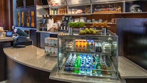 Een ontbijtbuffet met diverse dranken en fruit, een koffieapparaat en een menubord erboven.