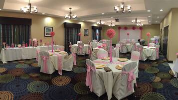 A banquet hall with round tables, chairs, and floral centerpieces.