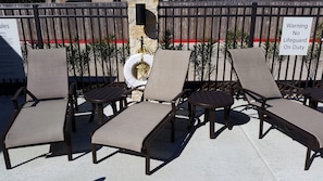 Des fauteuils de jardin sont disposés en demi-cercle, avec une clôture en bois et un panneau d’avertissement en arrière-plan.