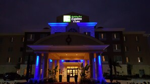 Edificio de Holiday Inn Express & Suites con un letrero llamativo, una entrada cubierta y un área frontal ajardinada.