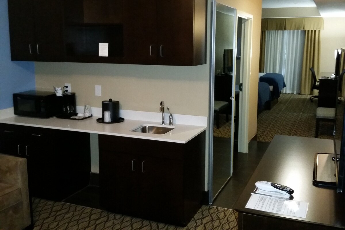 Una habitación de hotel compacta con kitchenette, cama, escritorio y silla.