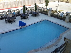 A rectangular pool with a diving board, surrounded by a black metal fence, and outdoor seating with tables and chairs. - Holiday Inn Express & Suites Atascocita - Humble - Kingwood by IHG (Humble)