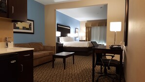 Habitación de hotel con cama, escritorio, sillón, mesa de noche, lámpara y un cuadro en la pared.