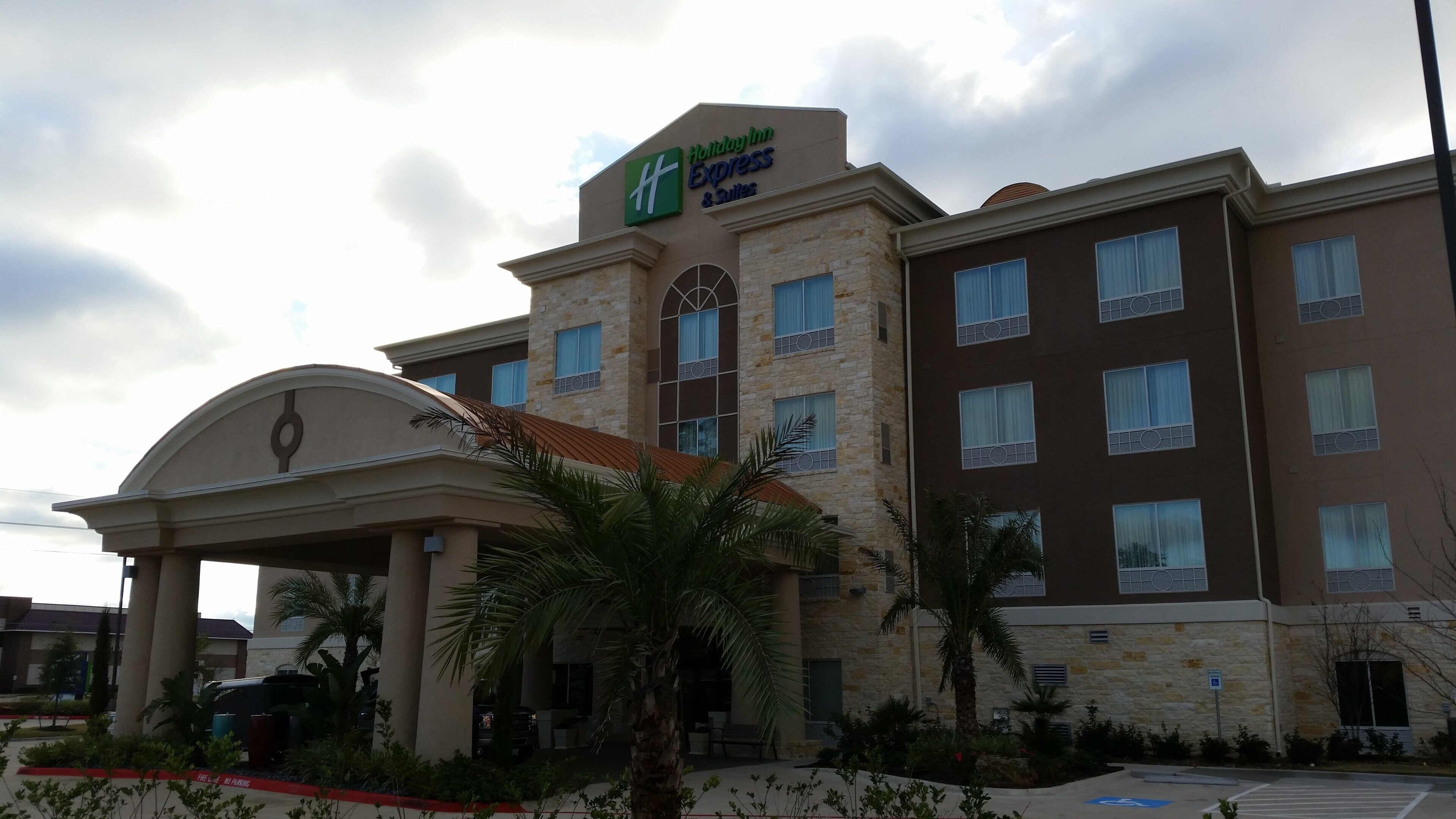 Een Holiday Inn Express & Suites gebouw met een stenen gevel, meerdere ramen en een centrale ingang met een decoratieve boog.