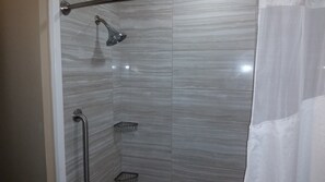 Ducha con cabezal de ducha de mano, barra de apoyo, estante pequeño y cortina de baño.