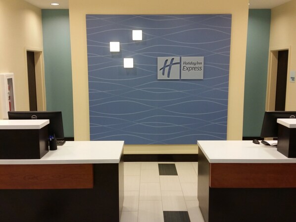 Un espace d’accueil avec un mur bleu orné d’un motif ondulé et du logo de Holiday Inn Express. On y trouve deux comptoirs d’accueil équipés d’ordinateurs et un sol carrelé.