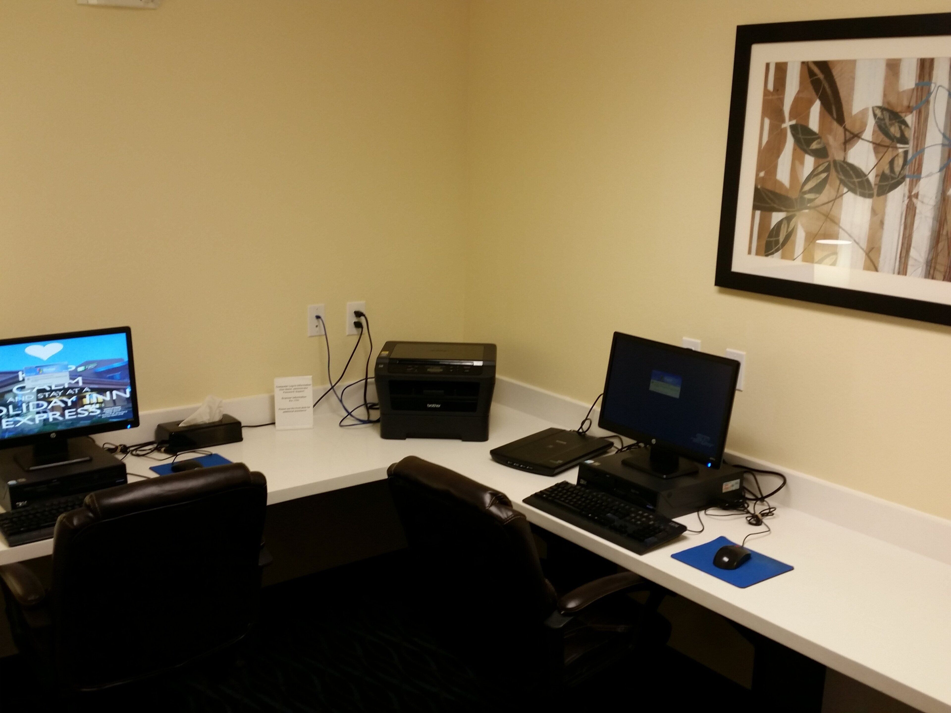A hotel office with two computer workstations, a printer, and a framed artwork on the wall.