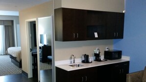 Una habitación de hotel con kitchenette, cama, escritorio y una silla.