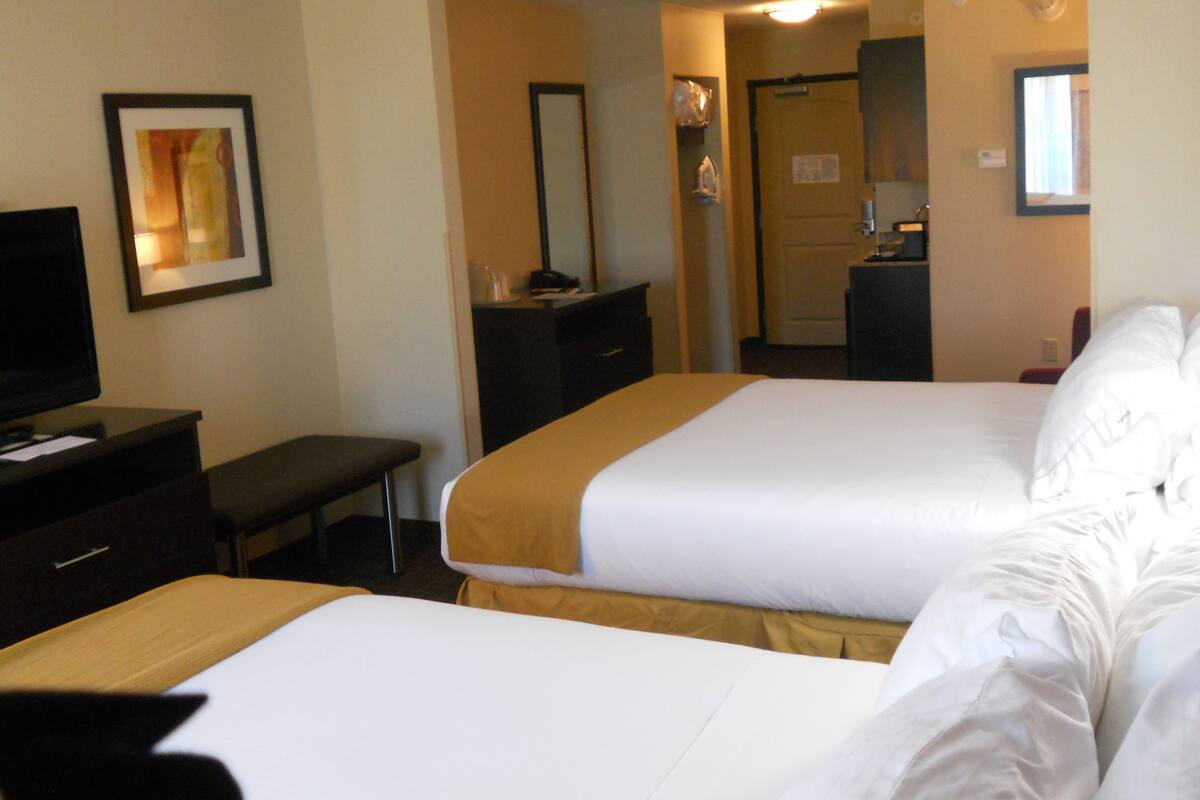 Une chambre d’hôtel avec deux lits, un bureau, une télévision et une salle de bain visible à travers une porte ouverte.