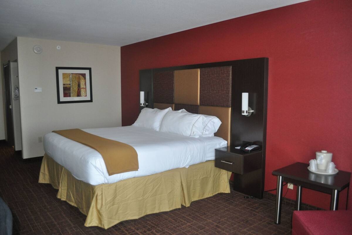 Une chambre d’hôtel avec un grand lit, une table de chevet, une petite table avec un plateau, et un mur rouge.