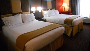 A hotel room with two beds, a red accent wall, a nightstand with a lamp, and a window with curtains. - Holiday Inn Express & Suites Greensburg by IHG (Greensburg)