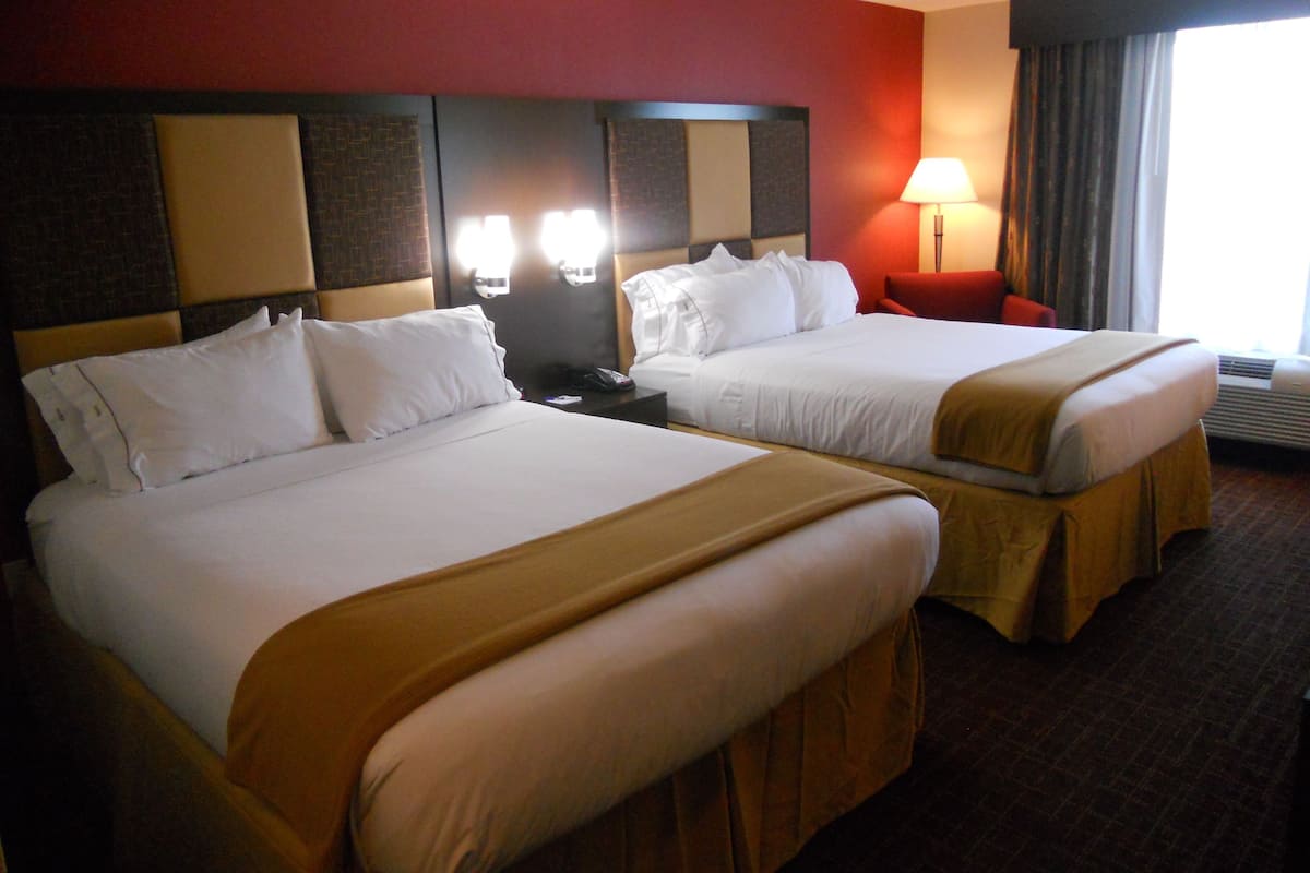 Une chambre d’hôtel avec deux lits, un mur d’accent rouge, une table de chevet avec une lampe et une fenêtre avec des rideaux.