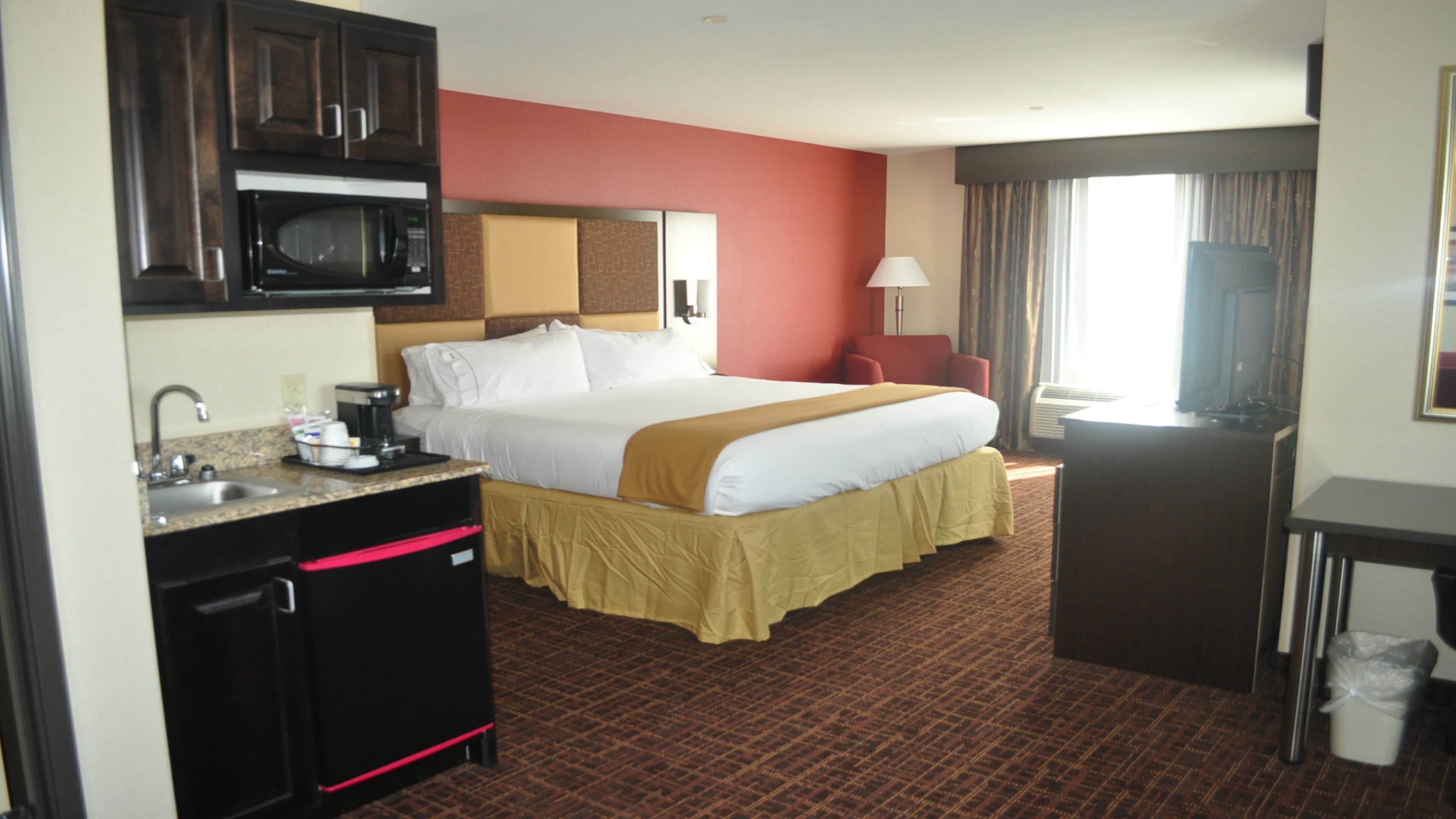 A hotel room with a bed, a desk, a microwave, a sink, and a television.