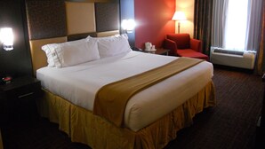 A hotel room with a large bed, a desk, a chair, a lamp, and an air conditioning unit. - Holiday Inn Express & Suites Greensburg by IHG (Greensburg)