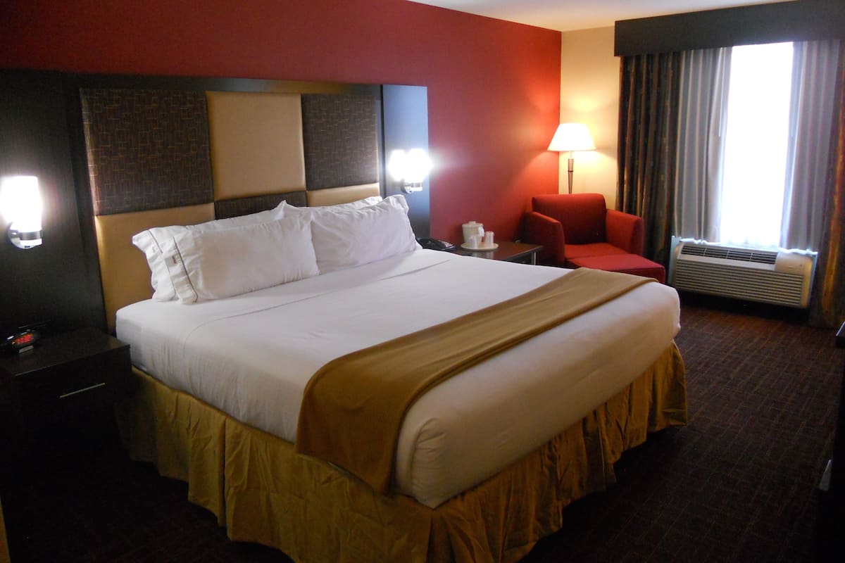 Une chambre d’hôtel avec un grand lit, un bureau, une chaise, une lampe et un appareil de climatisation.