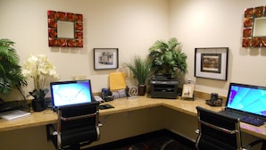 Un espace d’accueil d’hôtel comprenant deux postes de travail informatiques, une plante et des tableaux encadrés accrochés au mur.