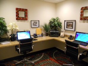 Un espace d’accueil d’hôtel comprenant deux postes de travail informatiques, une plante et des tableaux encadrés accrochés au mur.