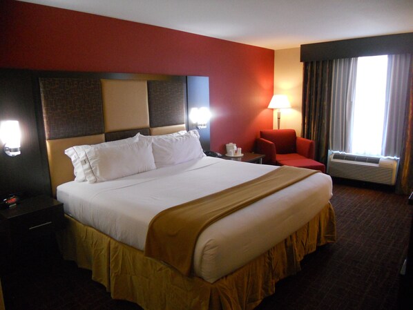 A hotel room with a large bed, a desk, a chair, a lamp, and a window with curtains.