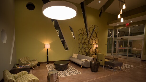 A modern lobby with a sofa, chairs, a coffee table, and a lamp. - Malana Hotels & Suites (Cotulla)