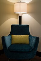 A dark blue armchair with a yellow cushion against a wall, under a floor lamp.