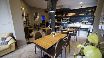 Un restaurant moderne avec des tables et des chaises en bois, un bar et une cuisine visible au fond de la salle.