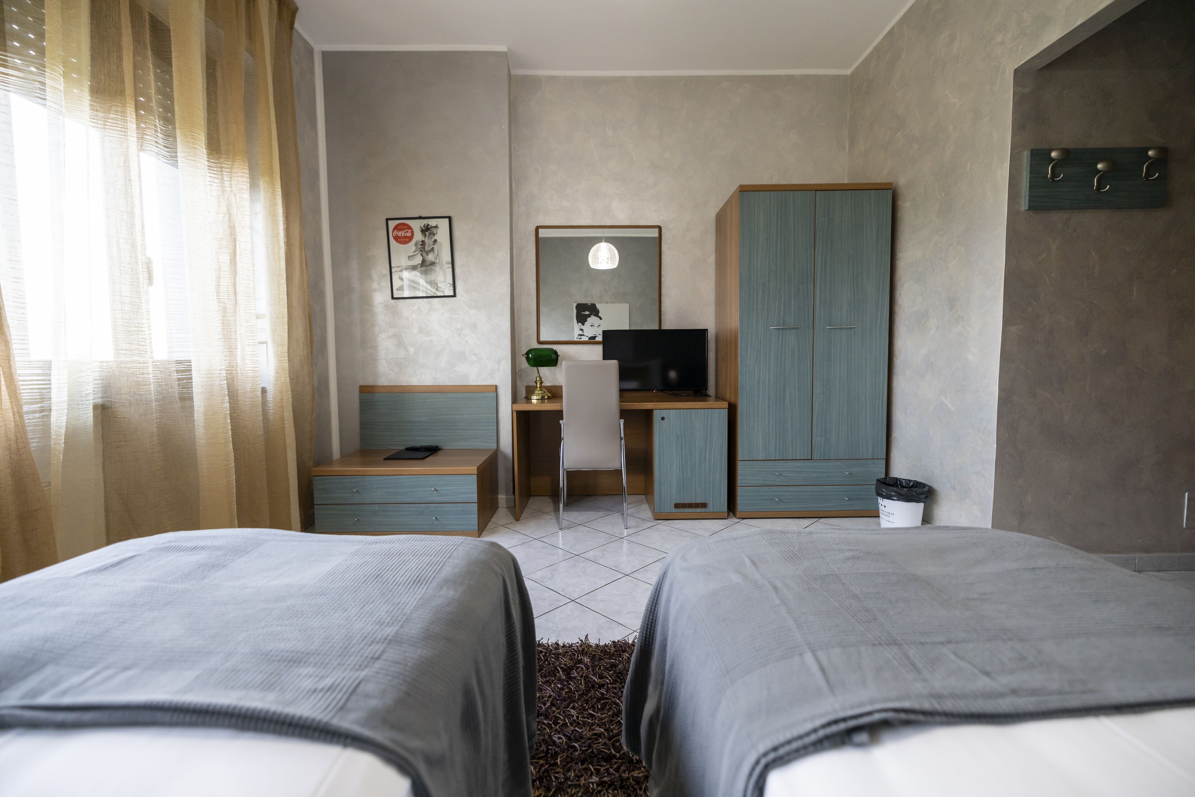 Une chambre d’hôtel avec deux lits, un bureau avec une chaise, une télévision et une armoire.