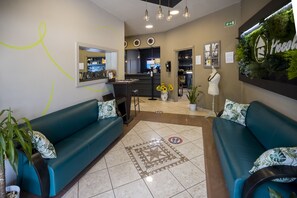 Un espace d’accueil avec des canapés de couleur turquoise, un sol à motifs et un mur vert orné d’un logo.