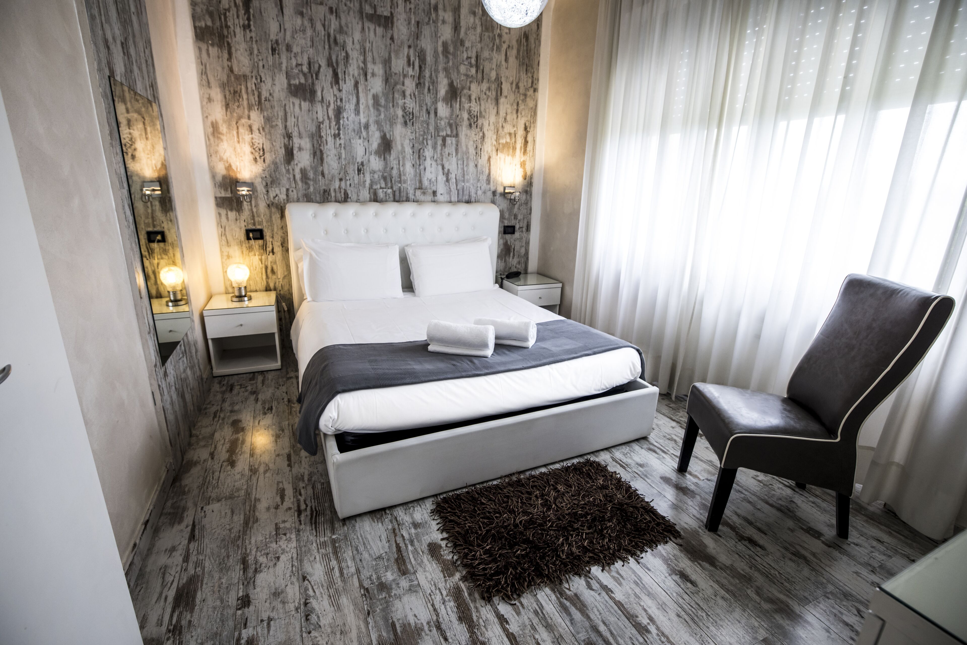 A modern bedroom with a large bed, bedside tables, a chair, and a textured wall.
