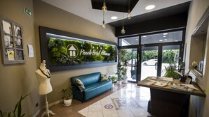 A reception area with a green wall, a blue sofa, a mannequin, and a reception desk. - Hotel Piccolo Allamano (Grugliasco)