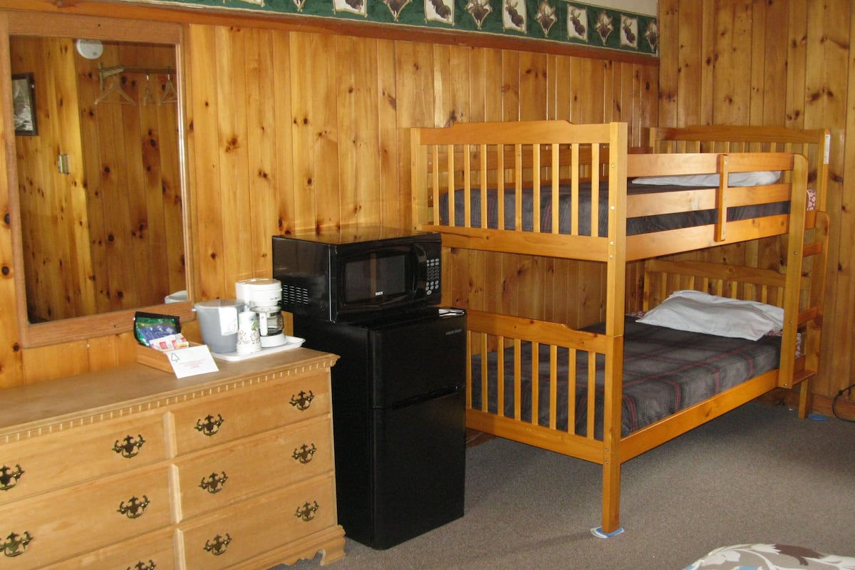 A bunk bed with a microwave and a coffee maker on a dresser, wooden walls, and a dresser with multiple drawers.