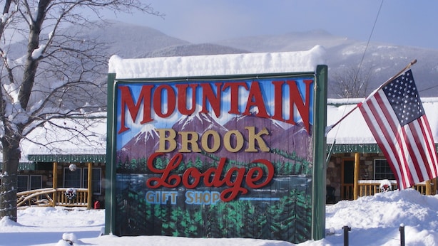 A sign for Mountain Brook Lodge with a gift shop, surrounded by snow and a mountain backdrop. - Mountain Brook Lodge (Wilmington)