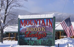 A sign for Mountain Brook Lodge with a gift shop, surrounded by snow and a mountain backdrop. - Mountain Brook Lodge (Wilmington)