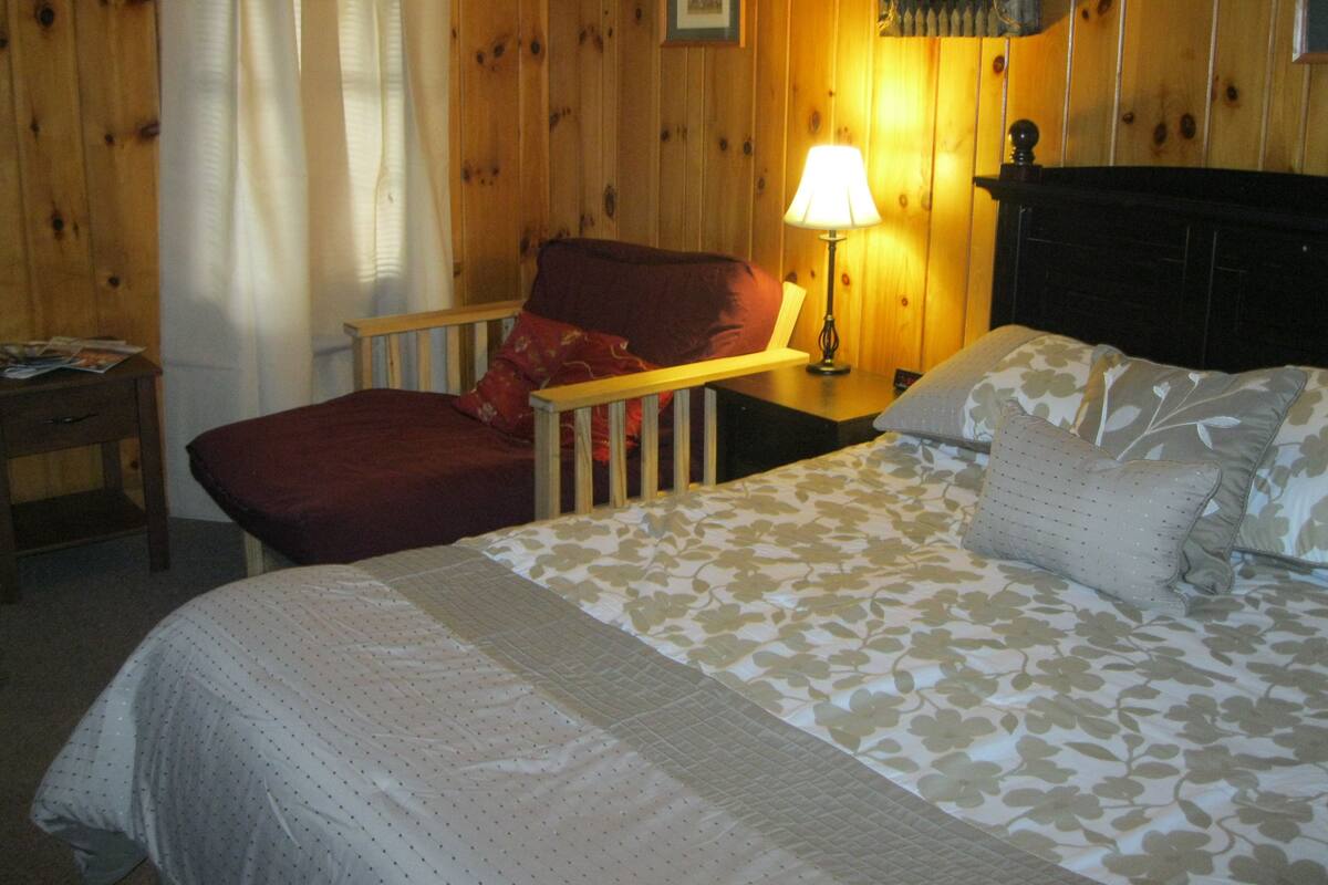 A cozy room with a bed, a chair, a nightstand, and a lamp.