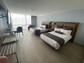 Une chambre d’hôtel avec un grand lit, un lit plus petit, un bureau avec une chaise et un balcon avec vue.