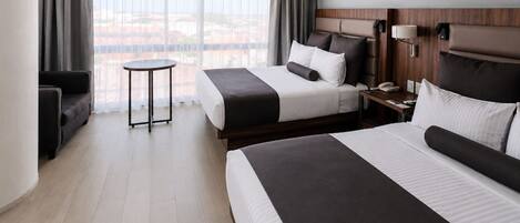 Habitación de hotel con dos camas, una mesita y vistas a la ciudad.