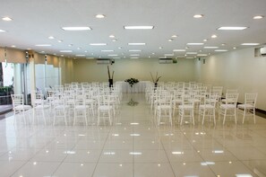 A spacious hall with rows of white chairs arranged for an event, a central floral arrangement, and a glass partition on one side. - Hotel Panorama (San Luis Potosi)