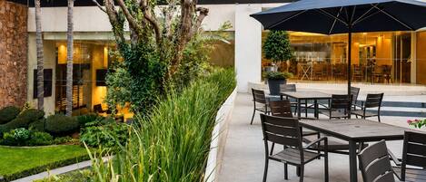 An outdoor patio with a table and chairs, surrounded by lush greenery and a stone wall.