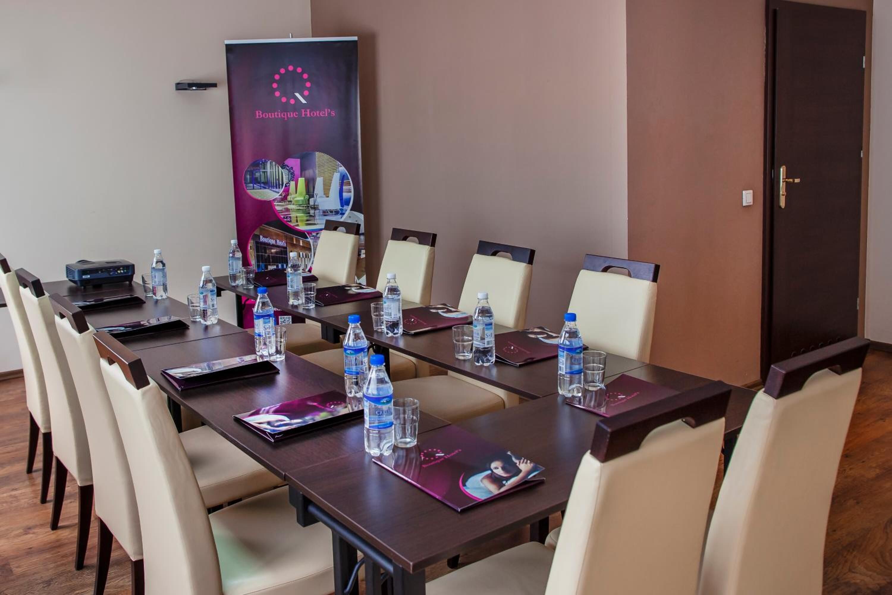 Ein Konferenzraum mit einem langen Tisch, Stühlen, Wasserflaschen und einem Banner für das Boutique Hotel.