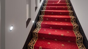 Un escalier recouvert d’une moquette rouge et orné de moulures noires, menant à un palier avec un mur blanc et une fenêtre.