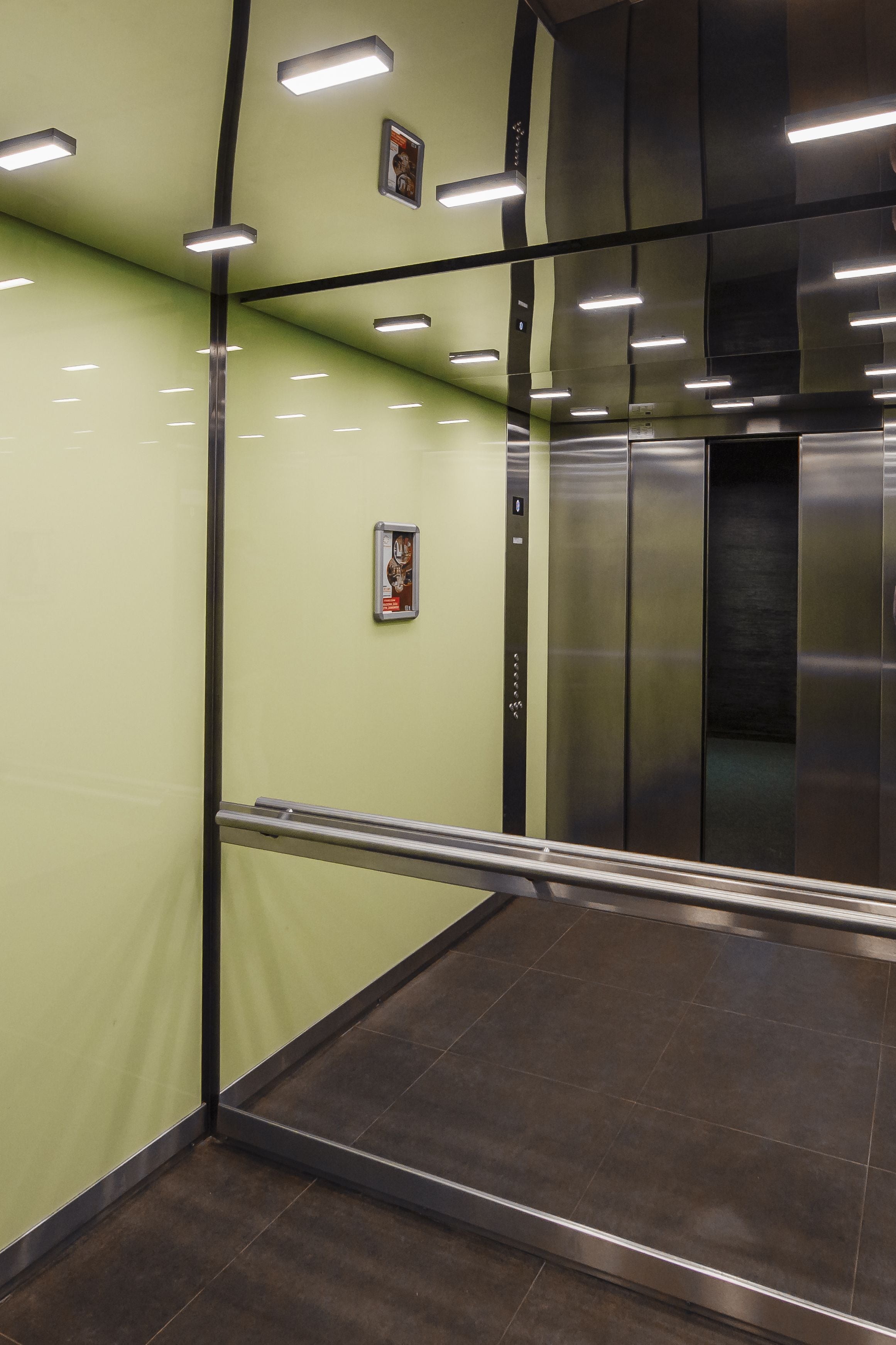 Vista interna di un ascensore con pareti metalliche, una ringhiera e illuminazione a soffitto.